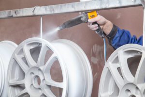 A person holding a spray gun applies a coating to tire rims.