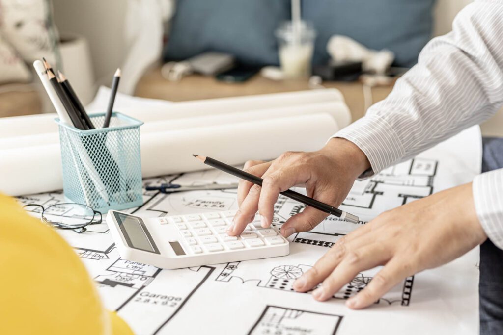 An architect is pressing keys on a calculator on top of blueprint drawings.