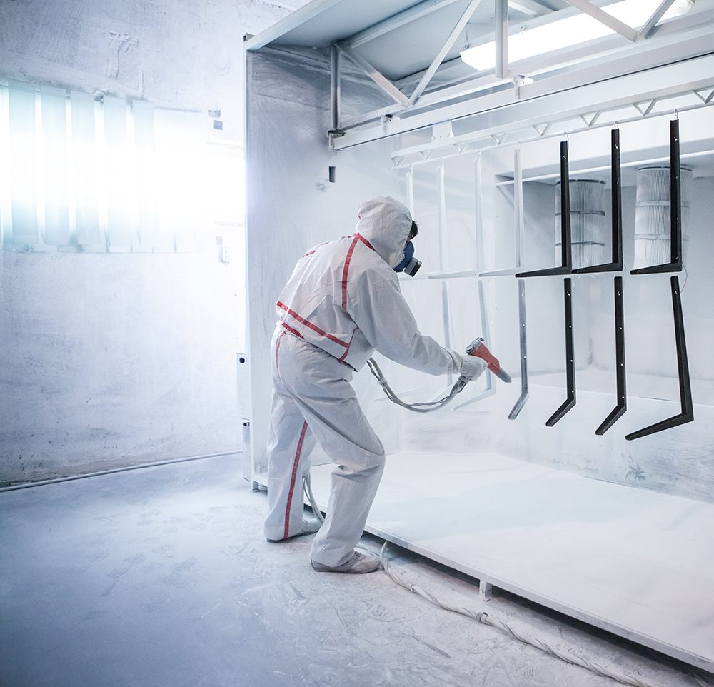 A person using a gun to powder coat metal parts.