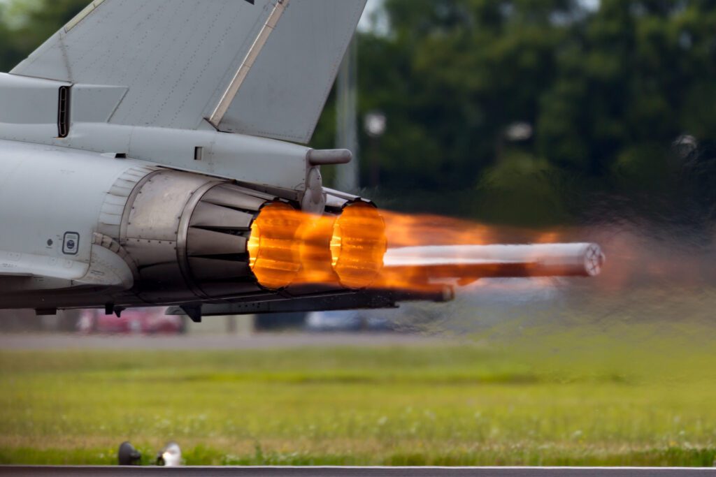 Afterburners glowing on an air force fighter jet as it speeds down the runway.
