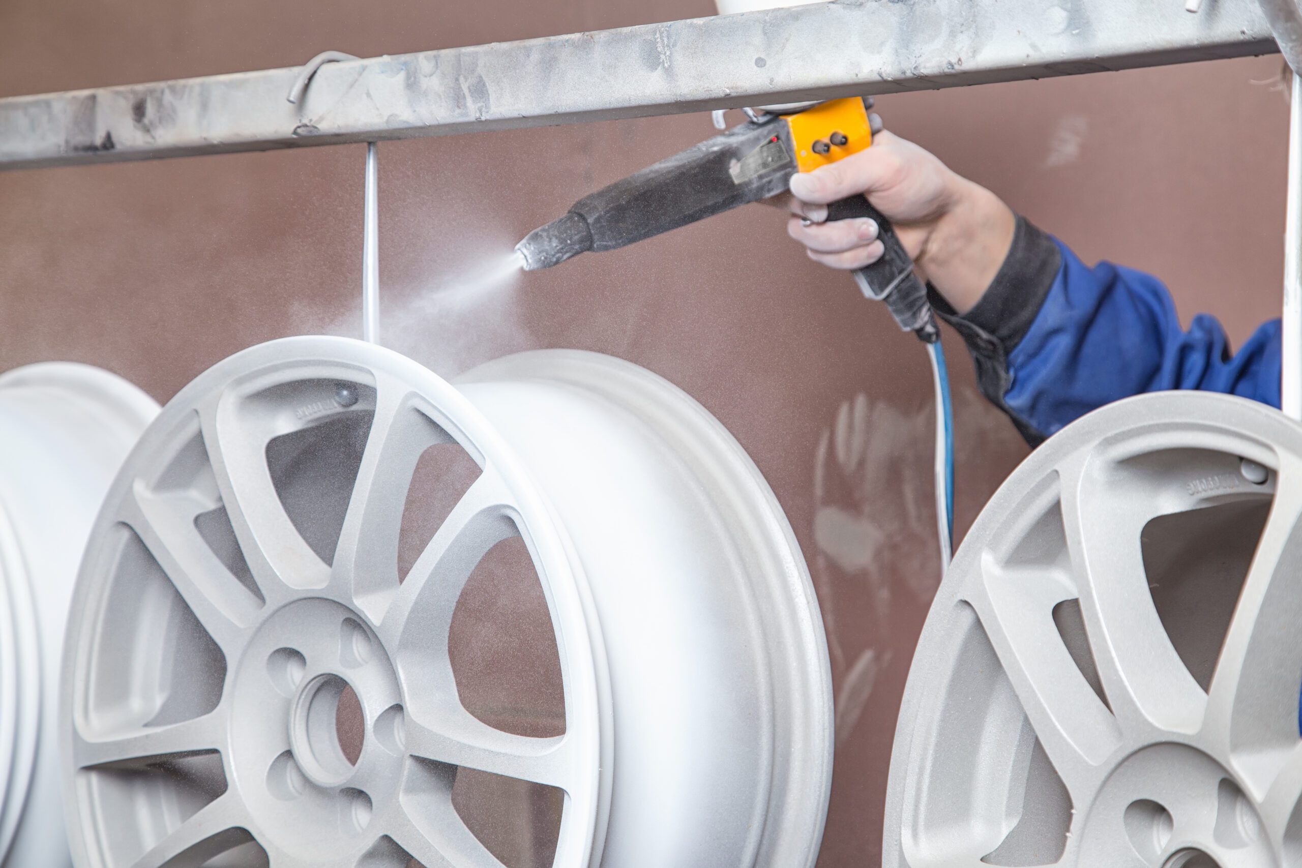 A person spraying a powder-coating gun onto a metal wheel.