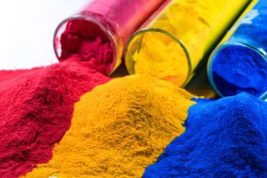 Tubes of pink, gold, and royal blue dry powder spill on a table.