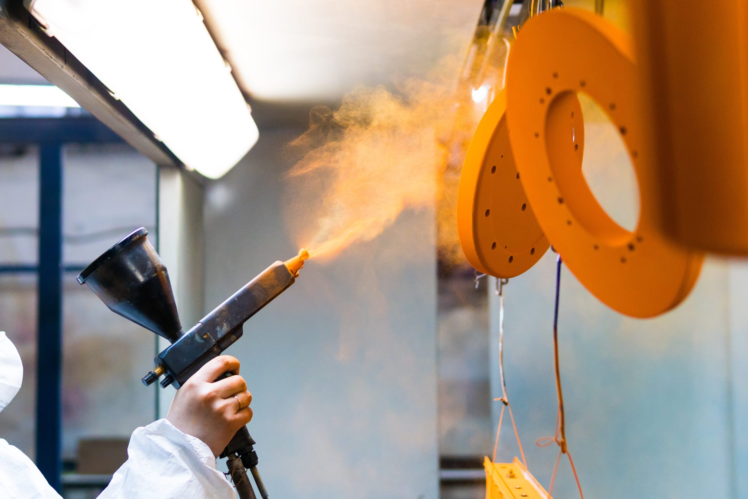 A person powder coats a metal object.