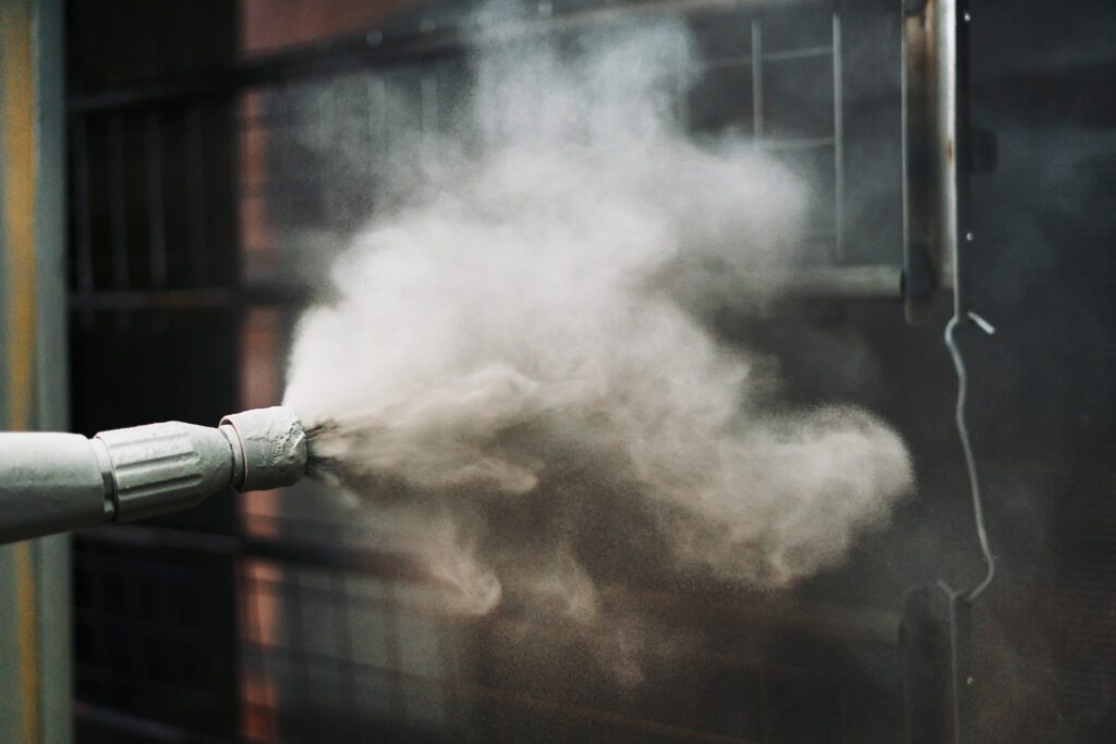 A powder spray gun blasting powder onto a metal object