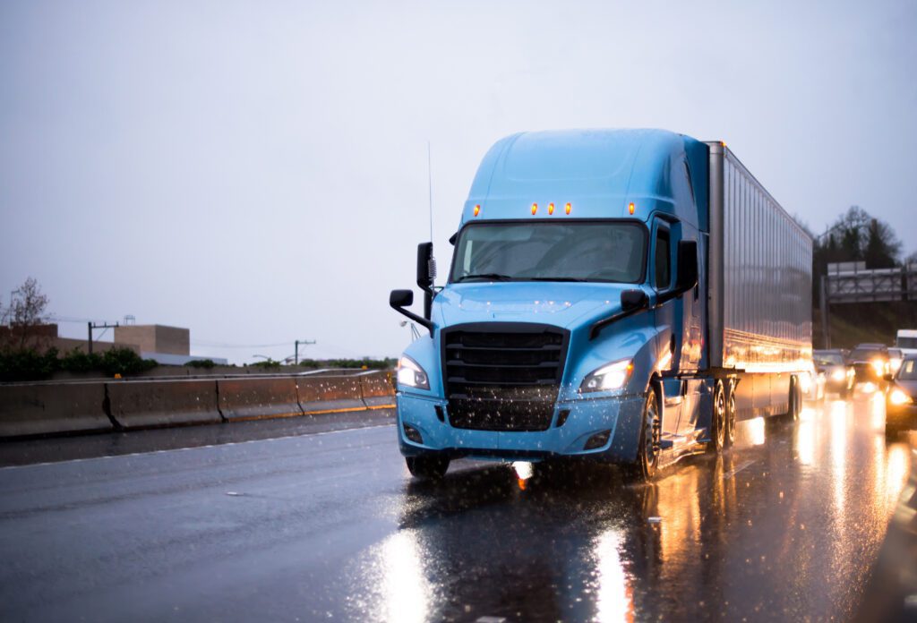 A blue tractor-trailer on the highway during the rain.