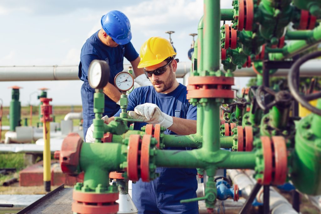 Men in hardhats tightening and checking piping at an oil field junction