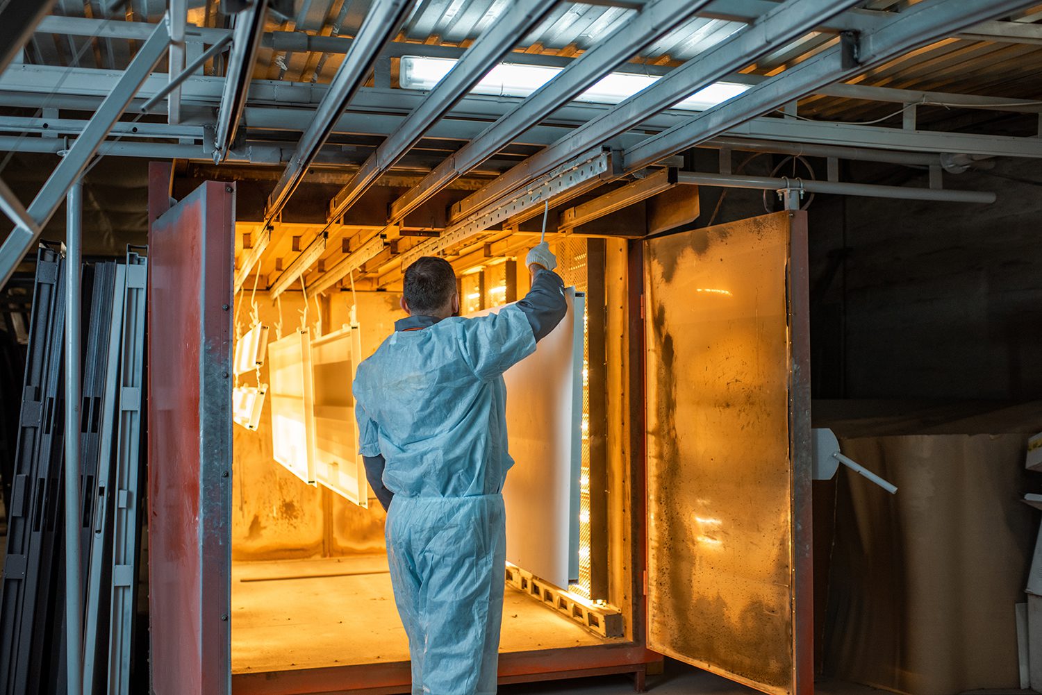 A powder coating tech in protection gear, guiding hanging parts into a powder coat oven.