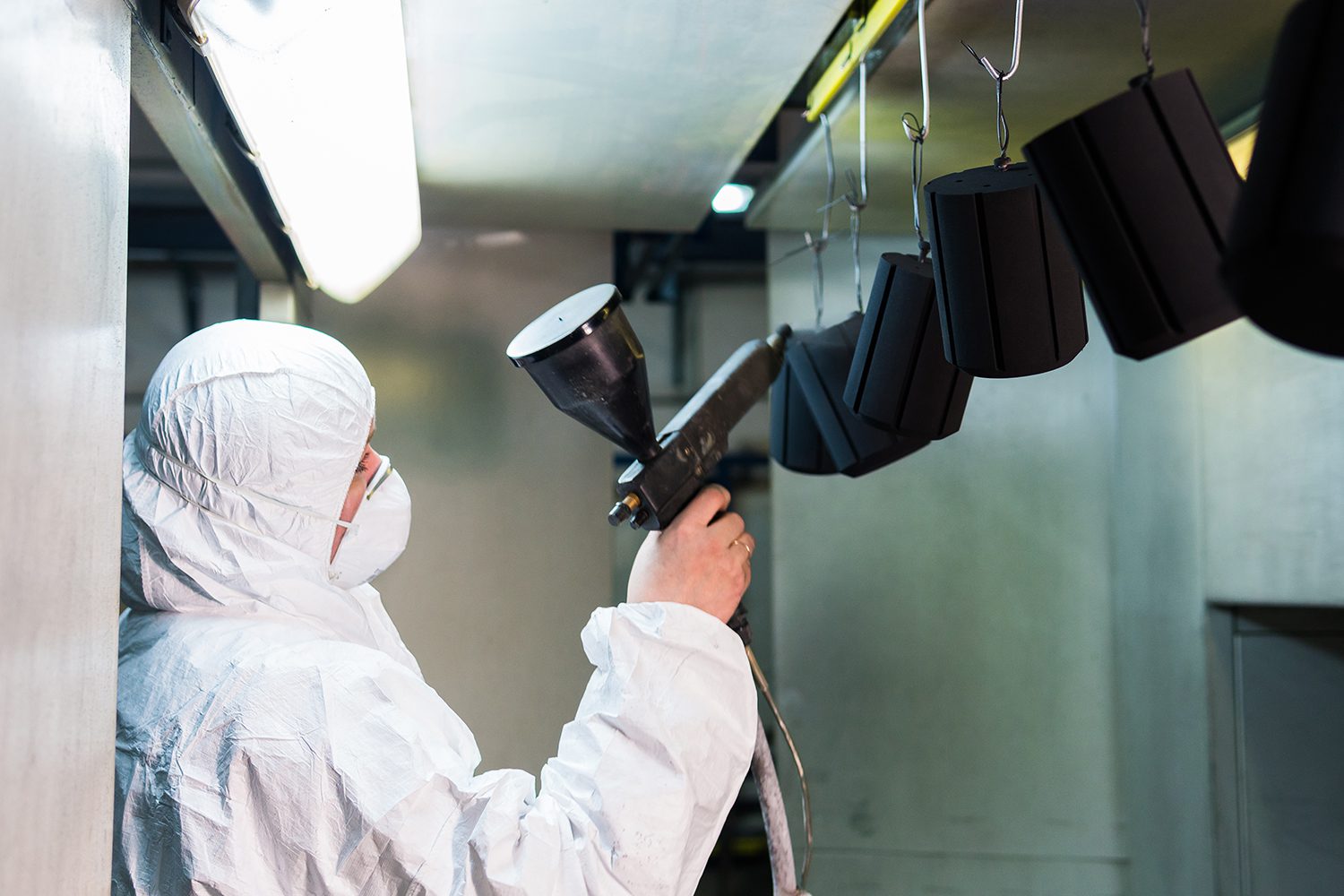 Man in a protective suit powder coating a metal piece.