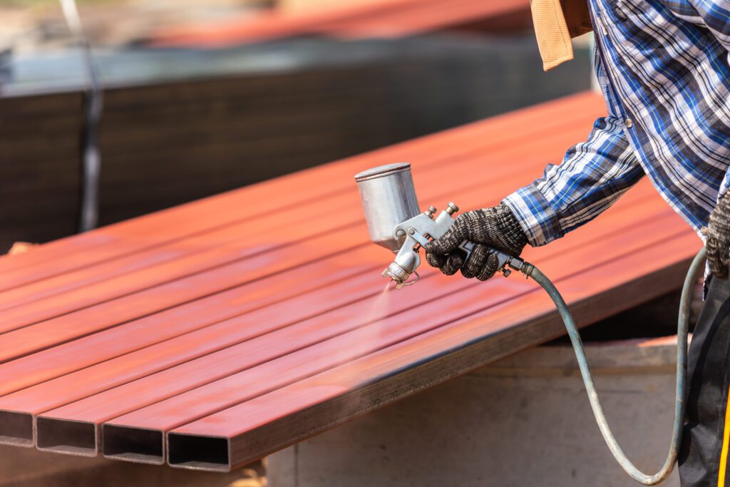 a worker spraying paint on a steel pipe to prevent rust 
