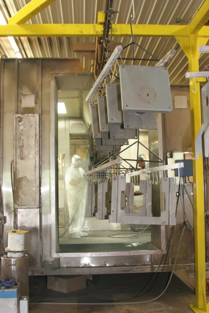 A person powder coating metal pieces on a conveyor.